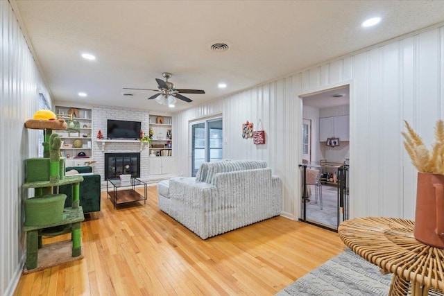 living room featuring ceiling fan, a brick fireplace, light hardwood / wood-style floors, and built in shelves