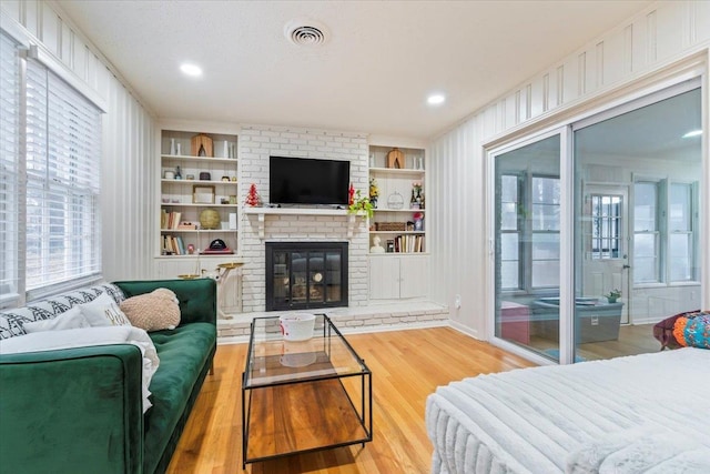 living room with a brick fireplace, built in features, and light wood-type flooring