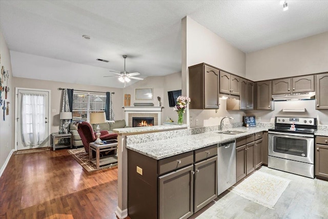 kitchen featuring a tile fireplace, appliances with stainless steel finishes, sink, kitchen peninsula, and light stone countertops