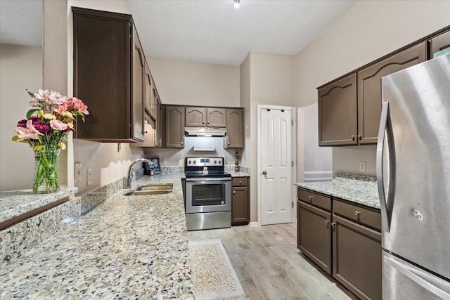 kitchen with appliances with stainless steel finishes, sink, dark brown cabinetry, light stone counters, and light wood-type flooring