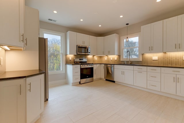 kitchen featuring sink, appliances with stainless steel finishes, white cabinetry, tasteful backsplash, and decorative light fixtures