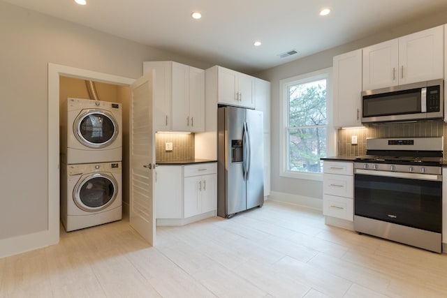 kitchen with stainless steel appliances, stacked washer and clothes dryer, white cabinets, and decorative backsplash