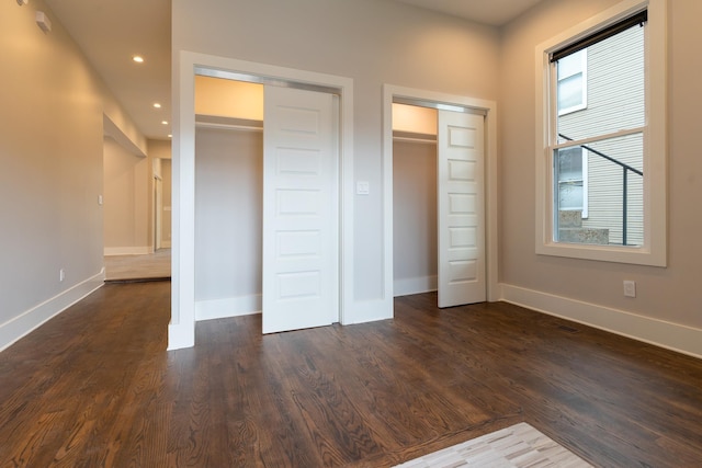 unfurnished bedroom featuring dark hardwood / wood-style flooring and two closets