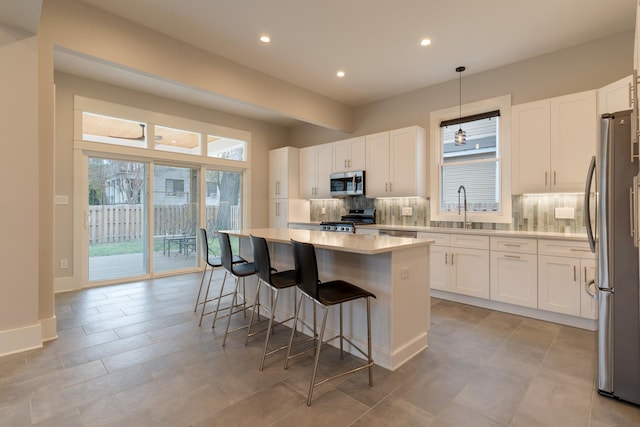 kitchen with stainless steel appliances, white cabinetry, a kitchen island, pendant lighting, and a healthy amount of sunlight