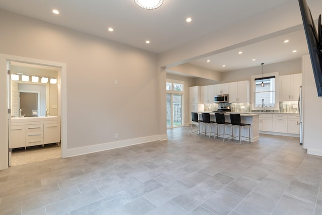 kitchen featuring a kitchen island, appliances with stainless steel finishes, white cabinets, a kitchen breakfast bar, and decorative backsplash