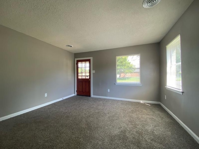 spare room with a textured ceiling and dark carpet