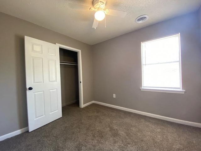 unfurnished bedroom with dark colored carpet, ceiling fan, a textured ceiling, and a closet