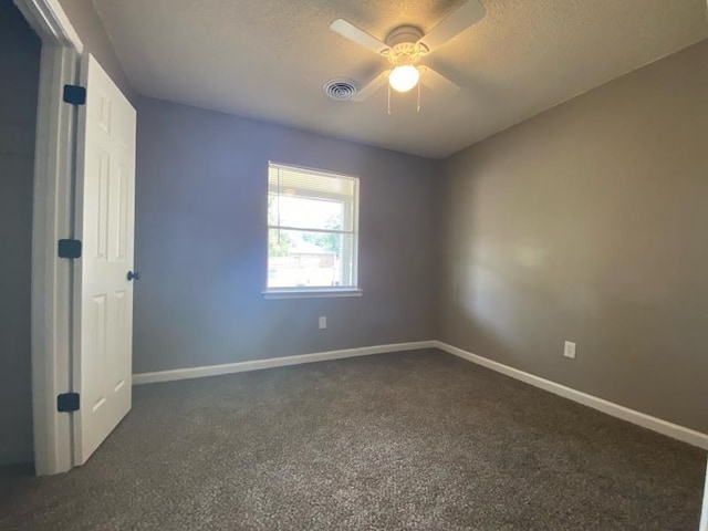 empty room featuring ceiling fan, dark carpet, and a textured ceiling