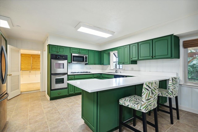 kitchen featuring light tile patterned flooring, a kitchen bar, green cabinetry, kitchen peninsula, and stainless steel appliances