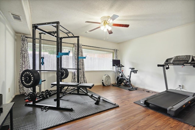 workout room with ceiling fan, ornamental molding, hardwood / wood-style floors, and a textured ceiling