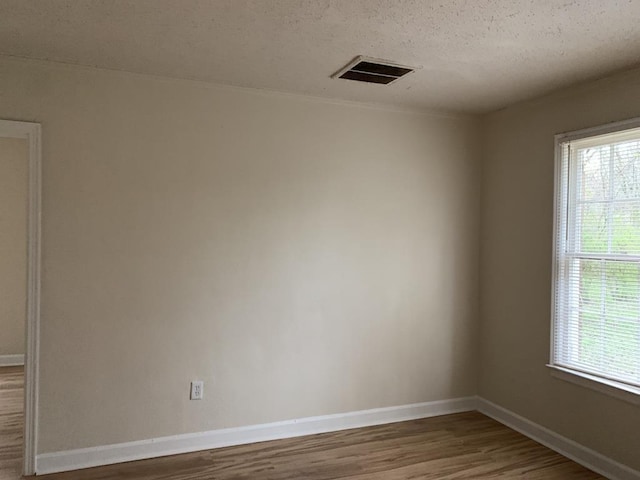 empty room featuring plenty of natural light, hardwood / wood-style floors, and a textured ceiling