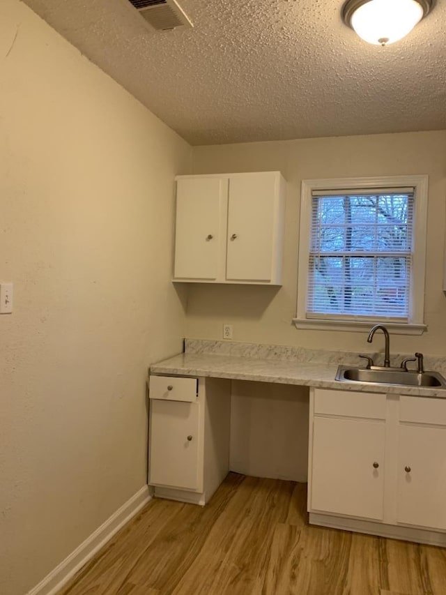 kitchen featuring sink, white cabinets, a textured ceiling, and light hardwood / wood-style flooring