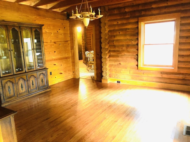 unfurnished dining area with beam ceiling, a chandelier, and hardwood / wood-style floors