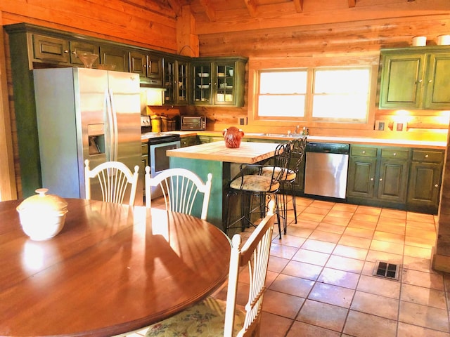 kitchen featuring lofted ceiling, appliances with stainless steel finishes, wooden walls, light tile patterned flooring, and wood counters