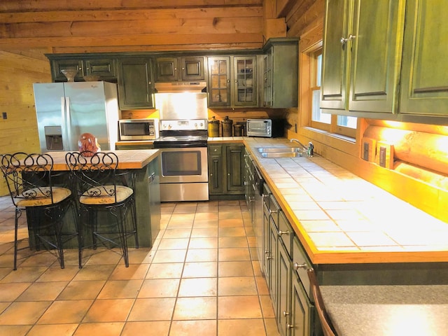 kitchen with sink, a breakfast bar area, appliances with stainless steel finishes, tile counters, and a kitchen island