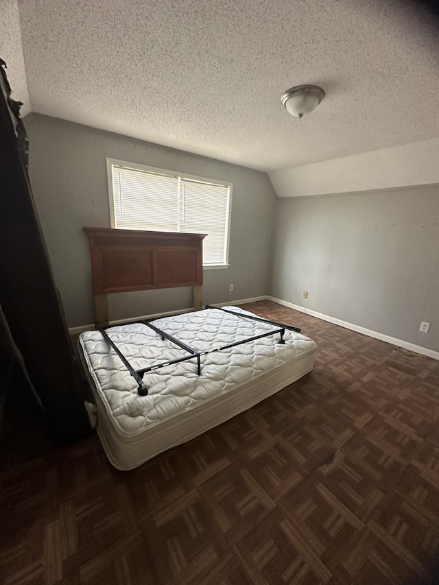 bedroom featuring dark parquet flooring, vaulted ceiling, and a textured ceiling