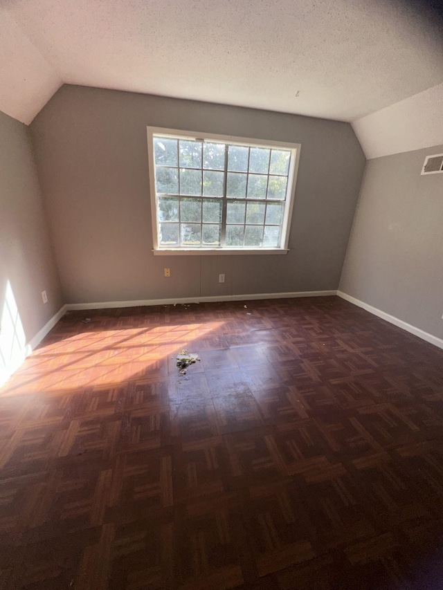 additional living space with lofted ceiling, dark parquet flooring, and a textured ceiling