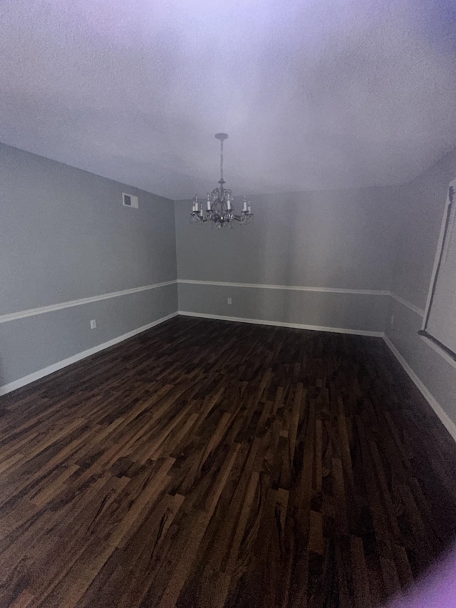 empty room featuring dark hardwood / wood-style floors, a chandelier, and a textured ceiling