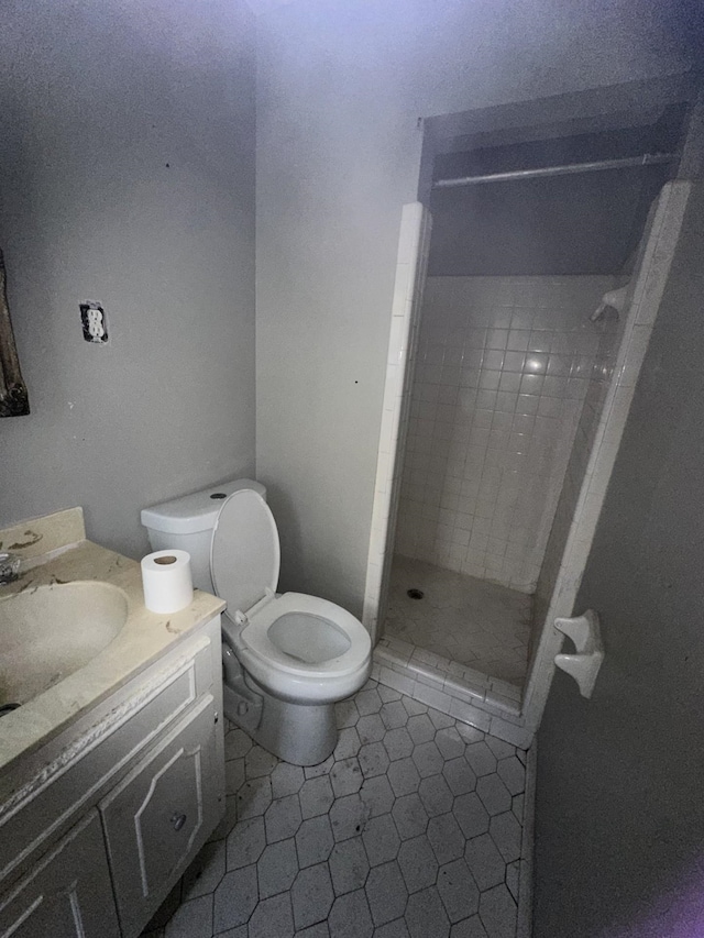 bathroom featuring a tile shower, vanity, tile patterned flooring, and toilet