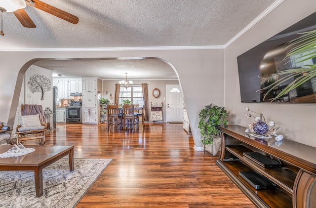 living room with dark hardwood / wood-style flooring, ceiling fan with notable chandelier, ornamental molding, and a textured ceiling