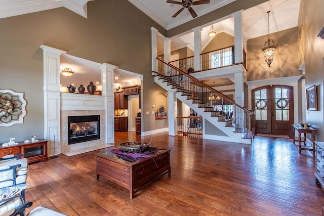 living room with crown molding, dark hardwood / wood-style floors, a tiled fireplace, and decorative columns