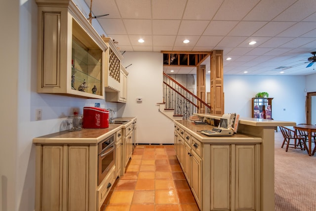 kitchen featuring sink, ceiling fan, a drop ceiling, light colored carpet, and stainless steel oven