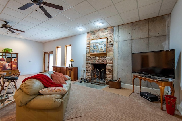 living room featuring a drop ceiling, a stone fireplace, light colored carpet, and ceiling fan