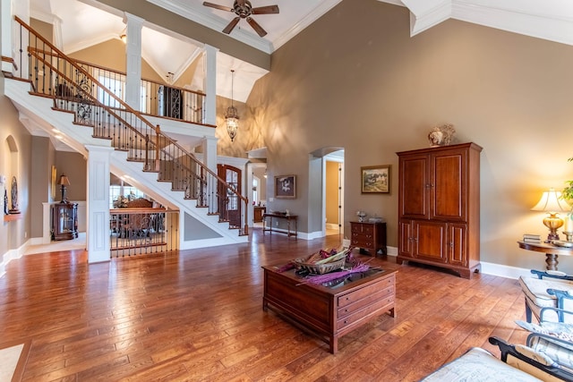 living room with ornate columns, wood-type flooring, high vaulted ceiling, ornamental molding, and ceiling fan