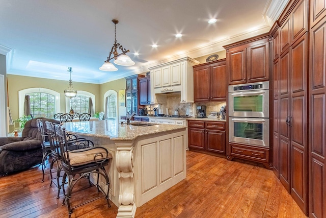 kitchen with a breakfast bar, wood-type flooring, a center island with sink, pendant lighting, and light stone countertops