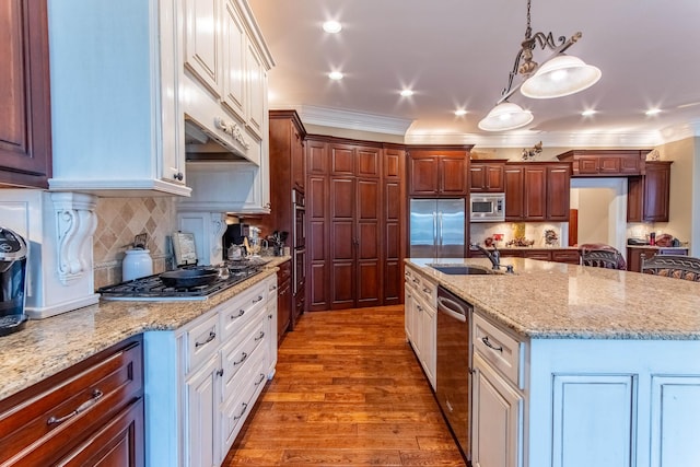 kitchen featuring sink, built in appliances, white cabinets, a center island with sink, and decorative light fixtures