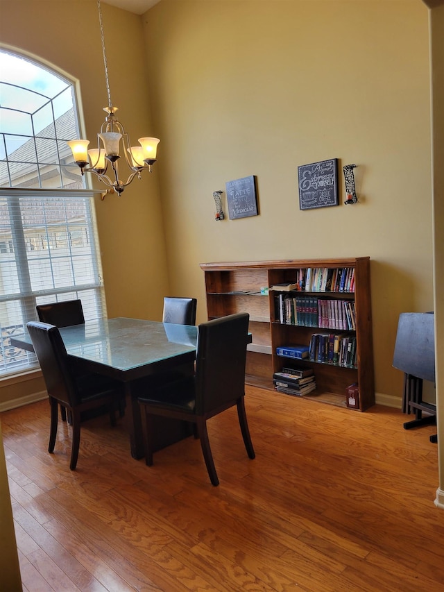 dining room featuring a towering ceiling, wood-type flooring, and a notable chandelier