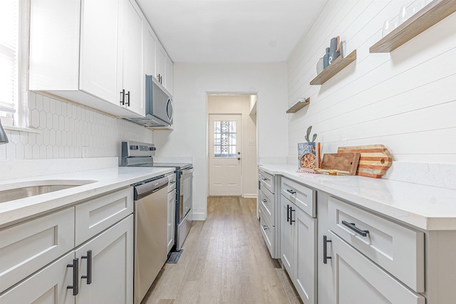 kitchen with appliances with stainless steel finishes, white cabinets, backsplash, light stone countertops, and light hardwood / wood-style flooring