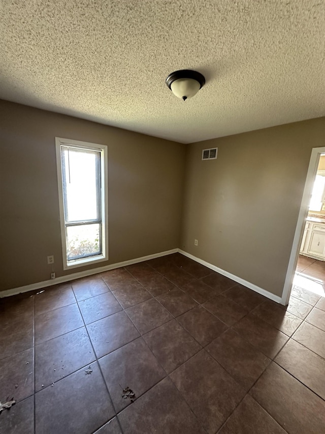 empty room with a textured ceiling and dark tile patterned floors