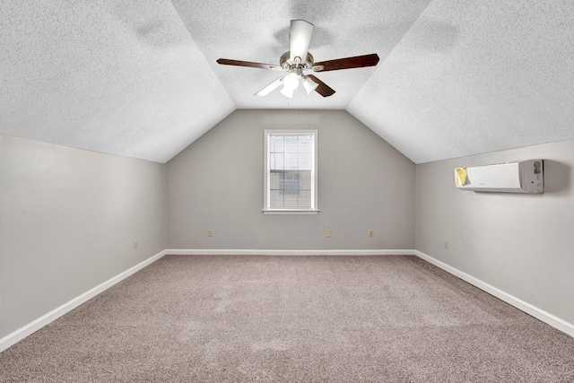 additional living space featuring lofted ceiling, ceiling fan, a wall unit AC, carpet, and a textured ceiling