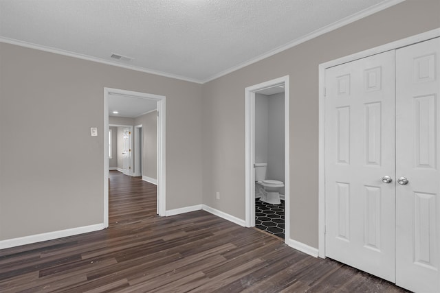 unfurnished bedroom with crown molding, ensuite bathroom, a textured ceiling, dark hardwood / wood-style flooring, and a closet