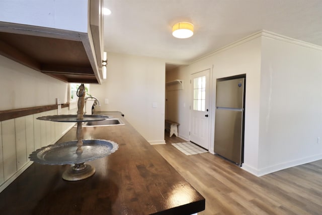 kitchen with stainless steel refrigerator, ornamental molding, sink, and light hardwood / wood-style flooring