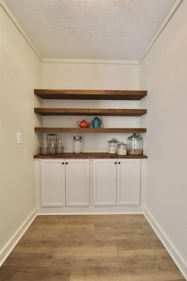 bar with white cabinetry, light hardwood / wood-style flooring, and a textured ceiling