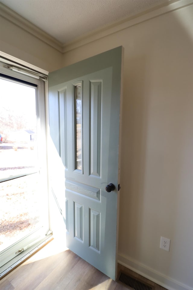 doorway featuring ornamental molding, a textured ceiling, and light wood-type flooring