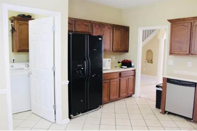 kitchen featuring washer / dryer, stainless steel dishwasher, light tile patterned floors, and black refrigerator with ice dispenser