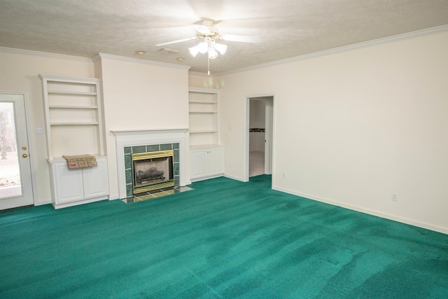 unfurnished living room with carpet floors, a tiled fireplace, ornamental molding, ceiling fan, and a textured ceiling