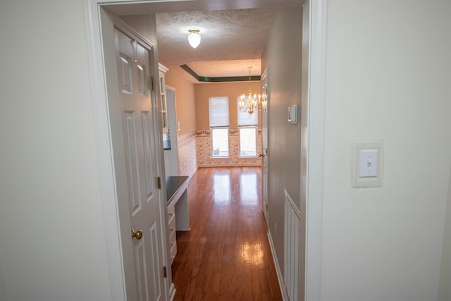 hall featuring dark hardwood / wood-style floors, a chandelier, a raised ceiling, and a textured ceiling