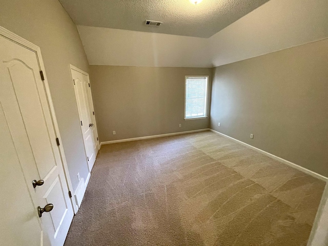 unfurnished bedroom featuring lofted ceiling, light carpet, and a textured ceiling