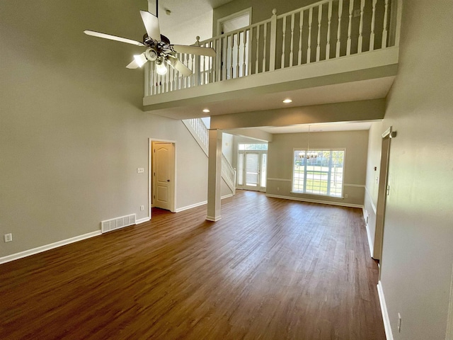 unfurnished living room with dark hardwood / wood-style floors, ceiling fan with notable chandelier, and a high ceiling