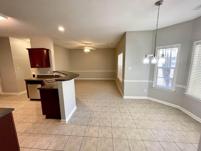 kitchen featuring pendant lighting, light tile patterned flooring, ceiling fan with notable chandelier, stainless steel dishwasher, and kitchen peninsula