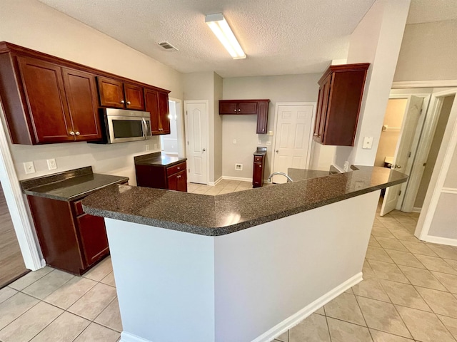 kitchen featuring light tile patterned flooring, a textured ceiling, and kitchen peninsula