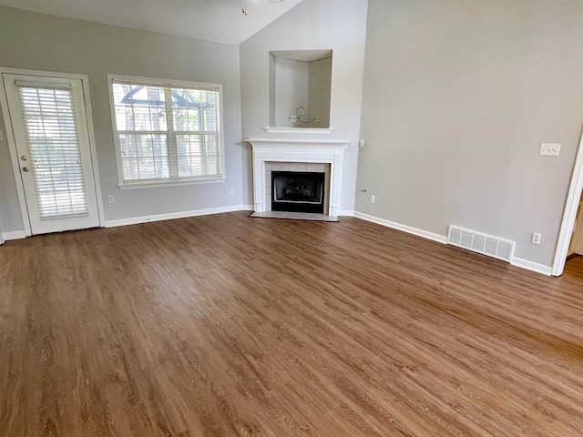 unfurnished living room with a tiled fireplace, dark wood-type flooring, and vaulted ceiling