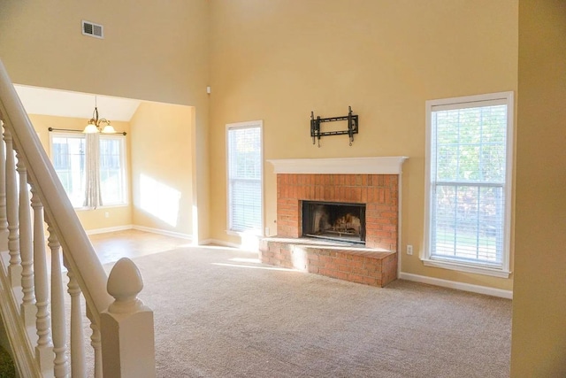 unfurnished living room with a brick fireplace, a notable chandelier, light colored carpet, and a high ceiling