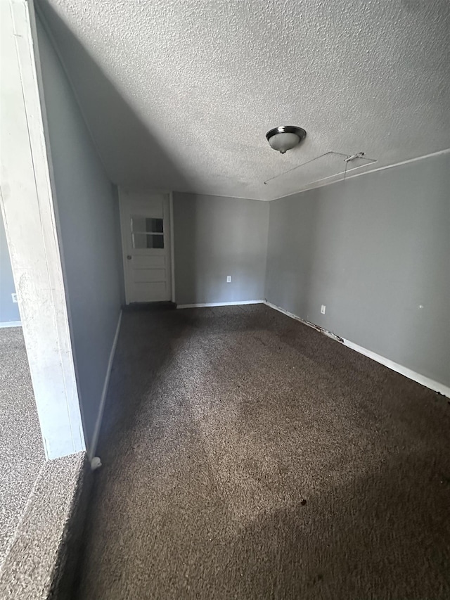 unfurnished room with dark colored carpet, baseboards, and a textured ceiling