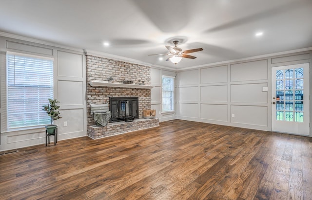 unfurnished living room with dark wood-type flooring, ceiling fan, ornamental molding, and a fireplace