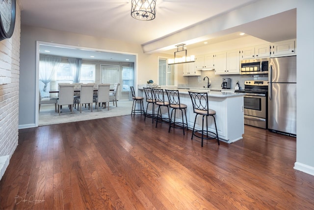 kitchen with decorative light fixtures, white cabinetry, a kitchen breakfast bar, kitchen peninsula, and stainless steel appliances